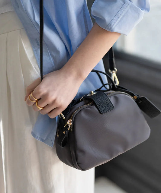 A female model is carrying a shoulder bag "Baby Nylon Loche" over her shoulder. Color: Gray Black (Gold-color hardware)