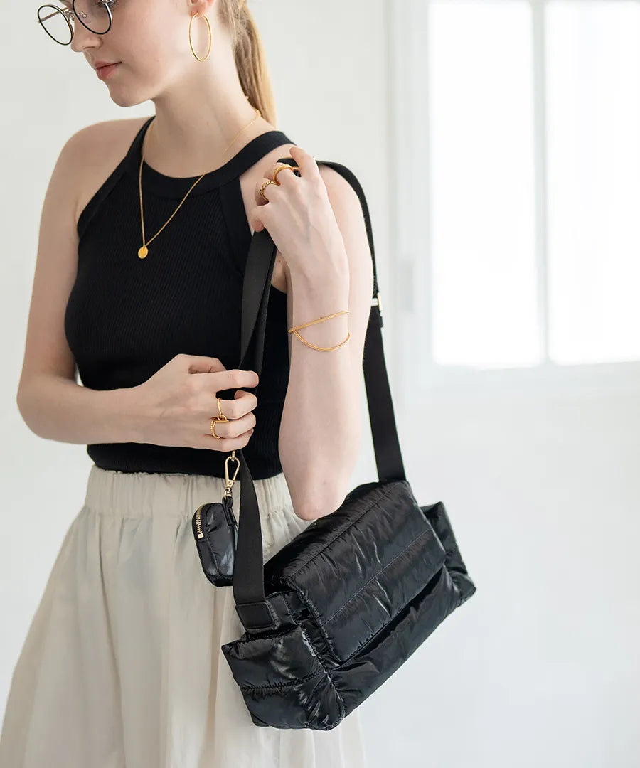 A female model is carrying a shoulder bag "Flaum" over her shoulder. Color:Black