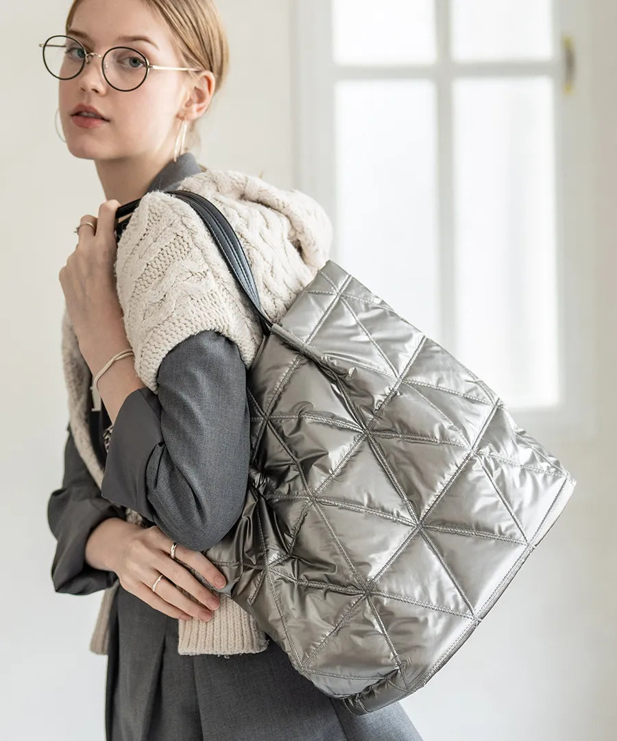 A female model is carrying a quilting tote bag "Trica" over her shoulder. Color:Silver