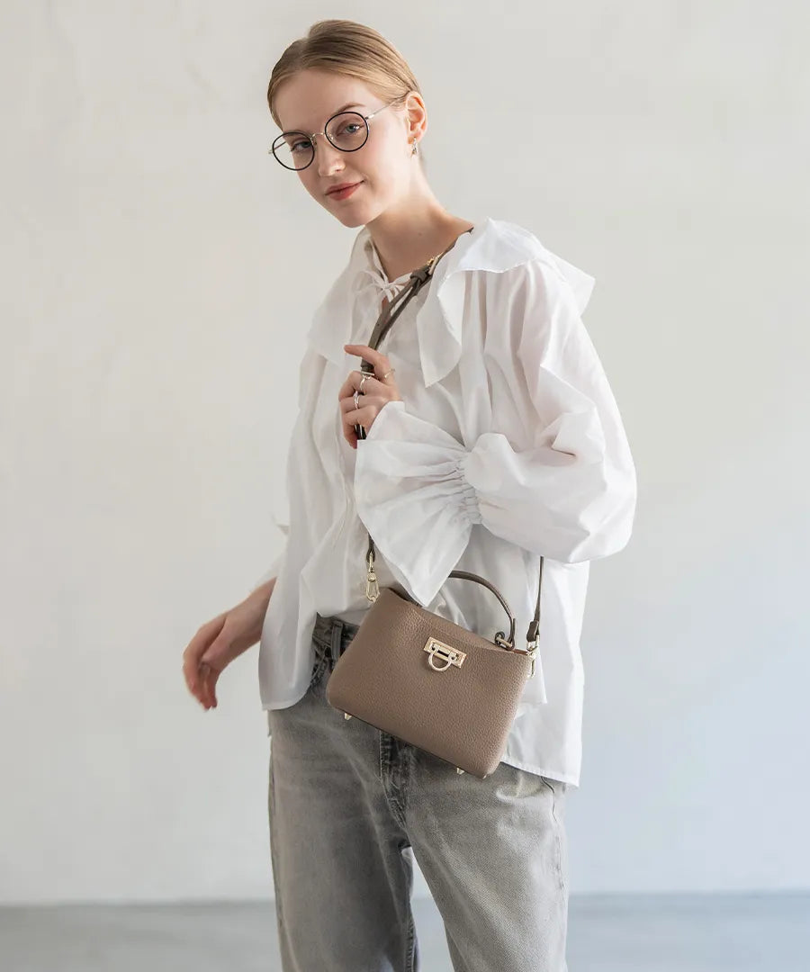 A female model is carrying a shoulder bag “Baby Marollet” over her shoulder. Color:Greige