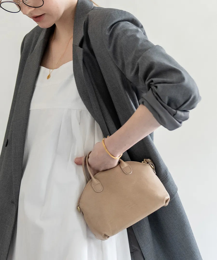 A female model is holding a bag "Light leather boston mini" Color:Sand greige