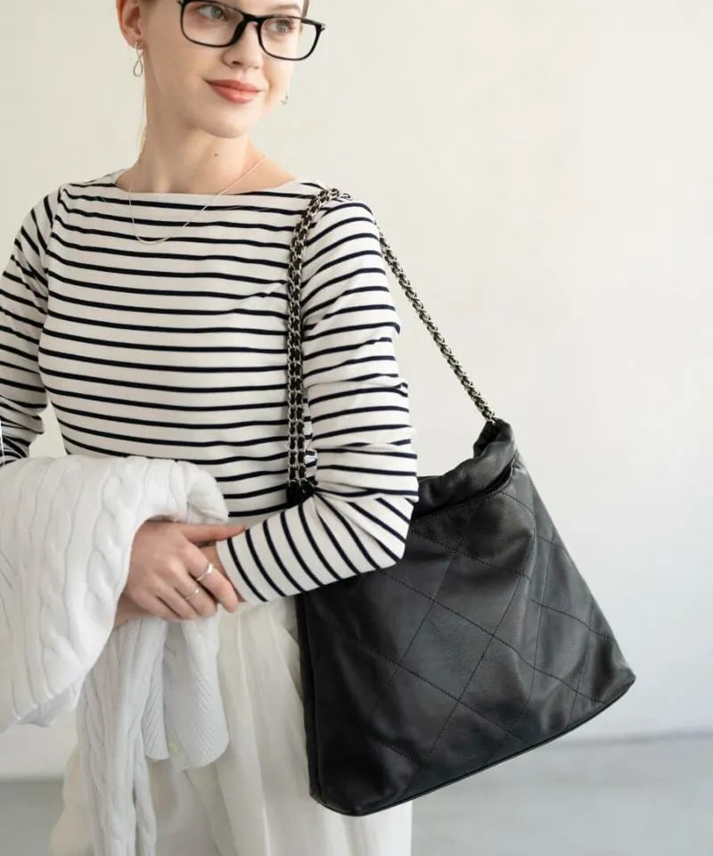 A female model is carrying a shoulder bag "Barmed" over her shoulder. Color:Black (Silver-color hardware)