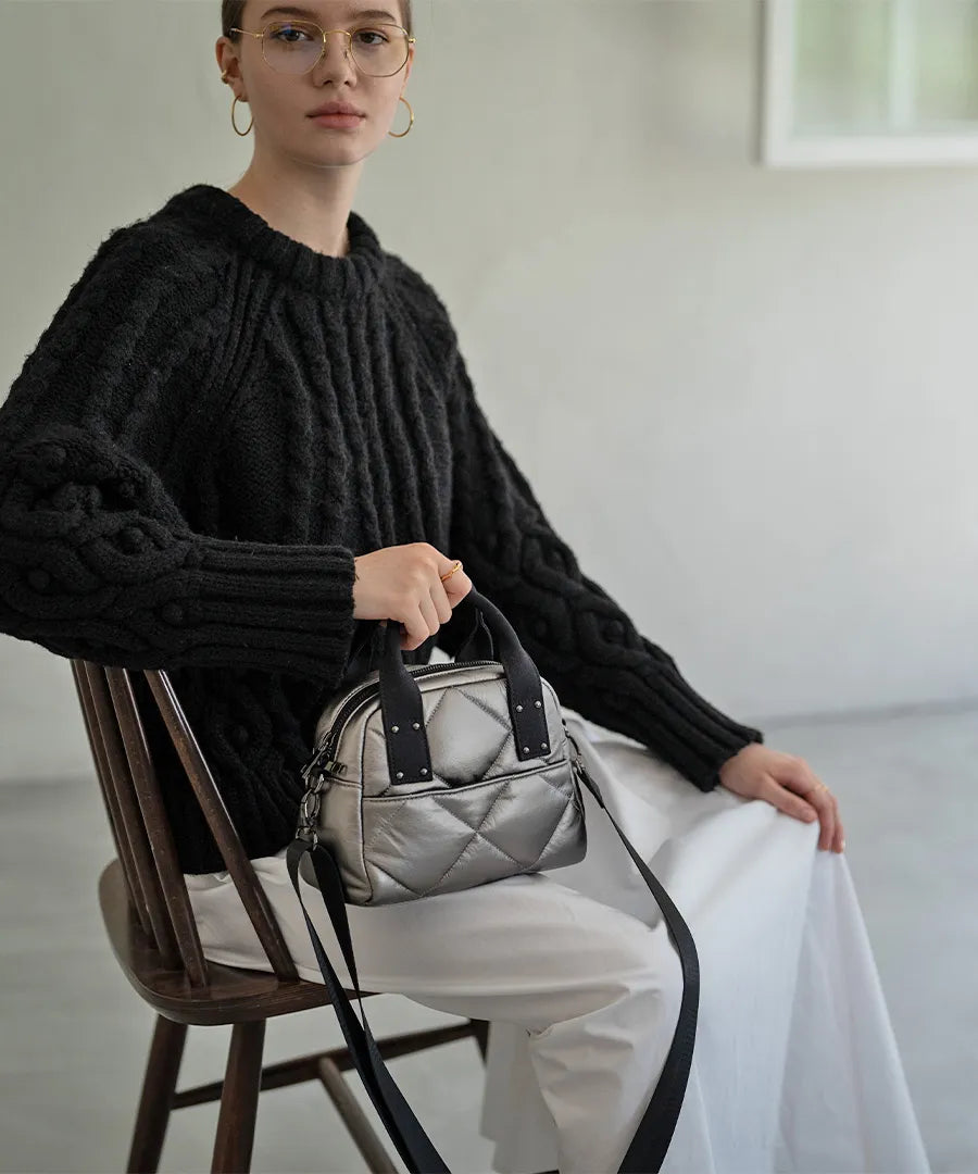 A female model is sitting and holding a hand bag "peremopetit".Color:Champagne silver