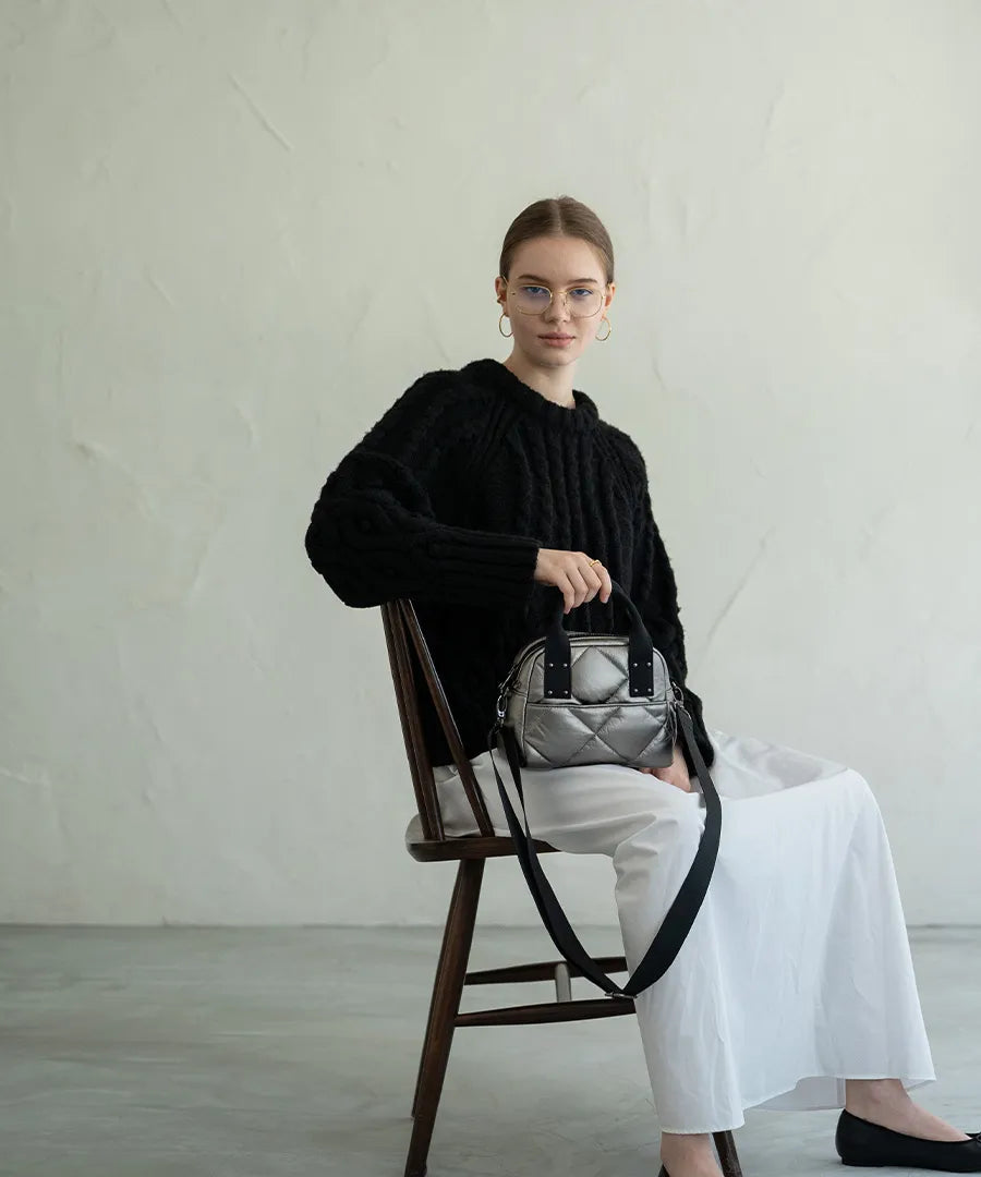 A female model is sitting and holding a hand bag "peremopetit".Color:Champagne silver