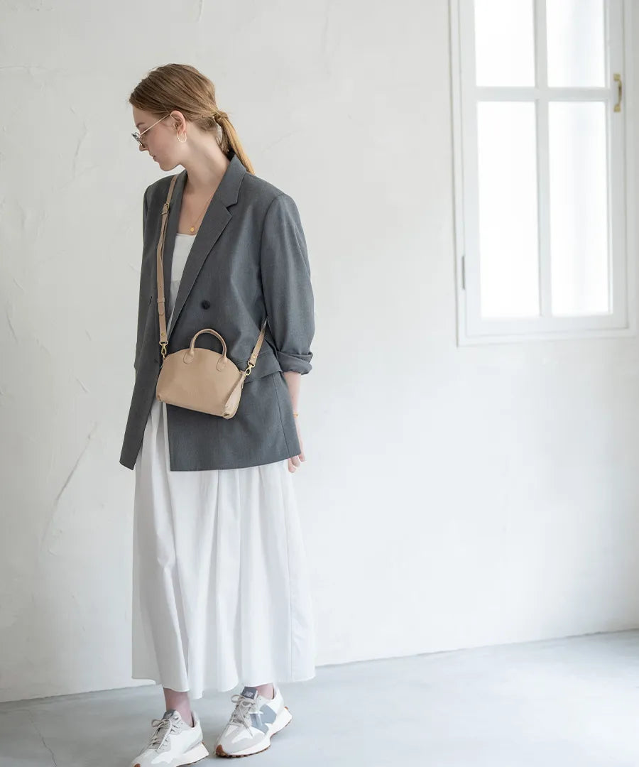 A female model is carrying a bag "Light leather boston mini" over her shoulder. Color:Sand greige