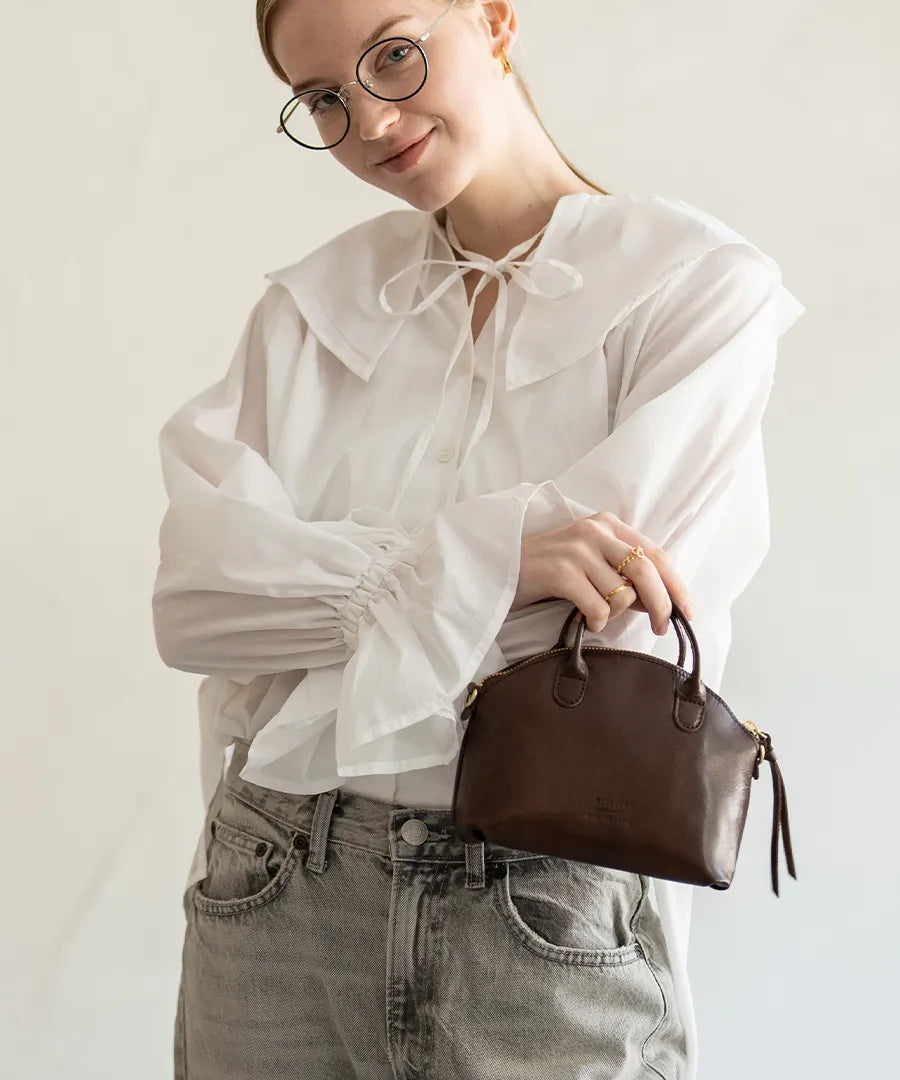 A female model is holding a bag "Light leather boston mini" Color:Chocolate brown