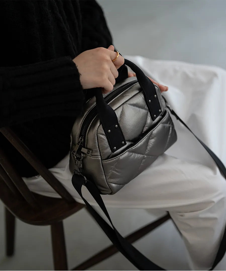 A female model is sitting and holding a tote bag "peremopetit".Color:champagne silver