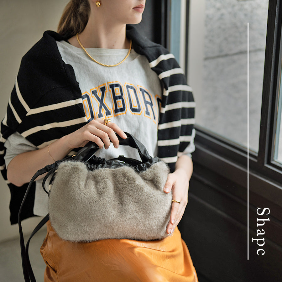 A female model is sitting and holding a tote bag "Dollfur". Color: Light gray
