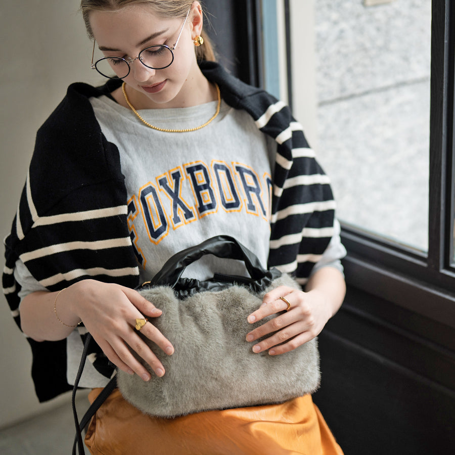 A female model is sitting and holding a tote bag "Dollfur". Color: Light gray