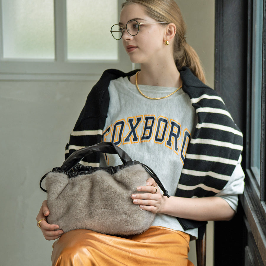 A female model is sitting and holding a tote bag "Dollfur". Color: Light gray