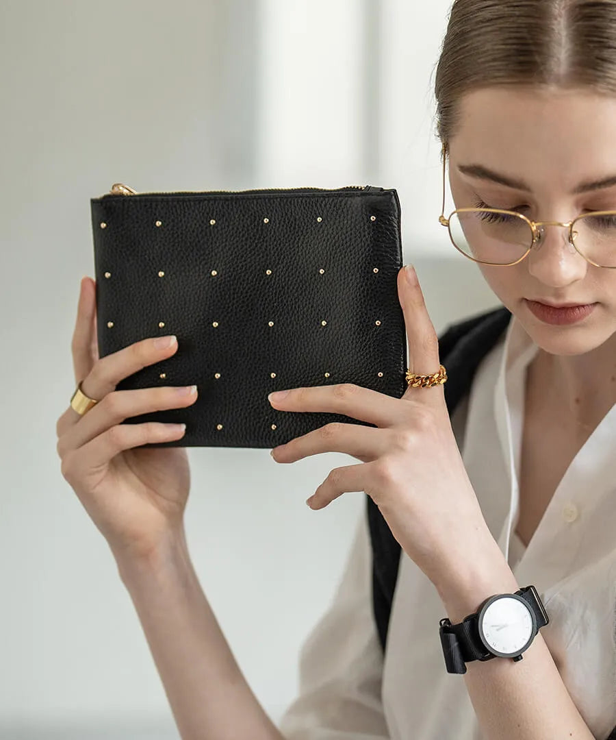 A female model is holding a leather pouch "Dotlpouch M" Color:Gold dot