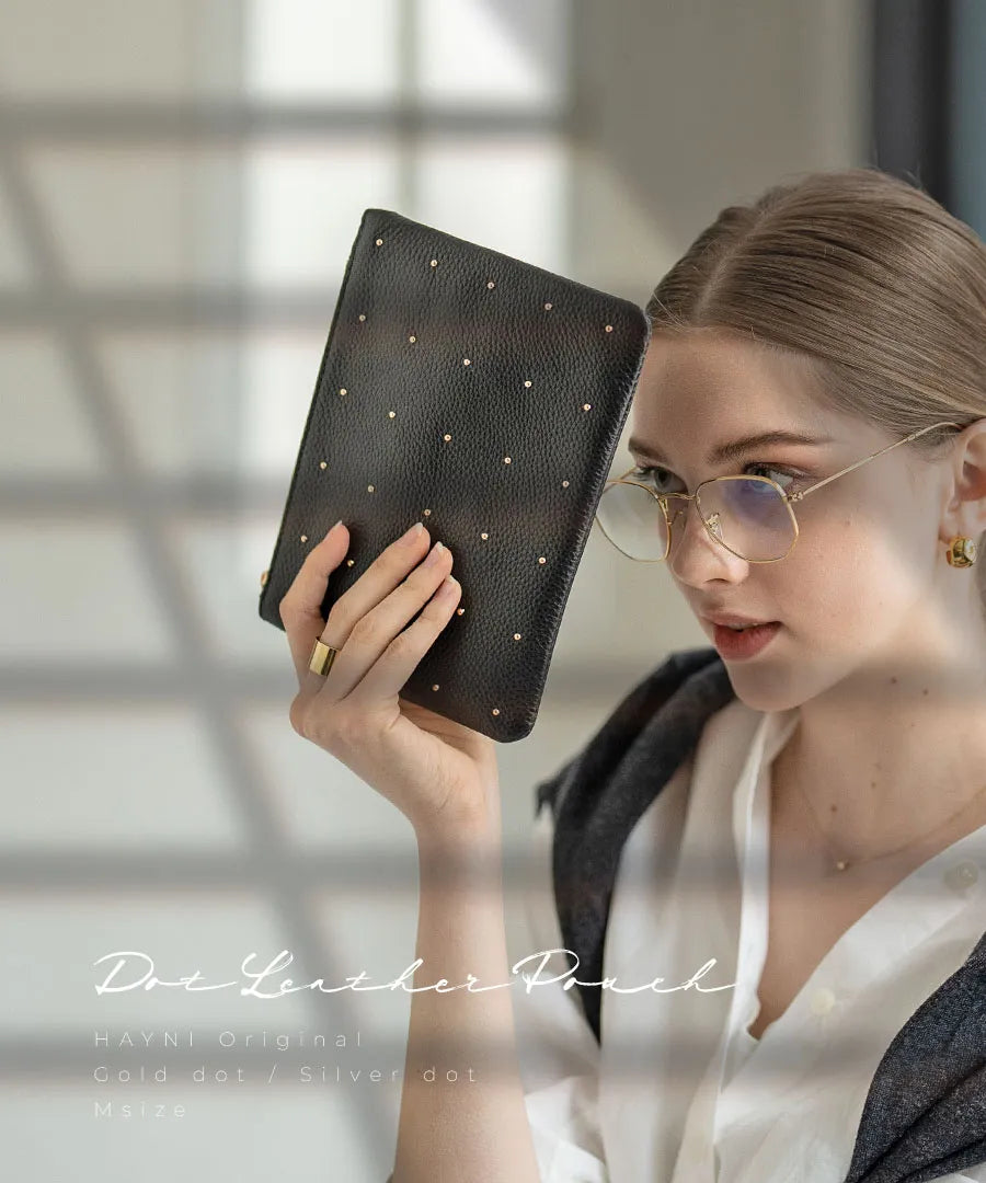 A female model is holding a leather pouch "Dotlpouch M" Color:Gold dot