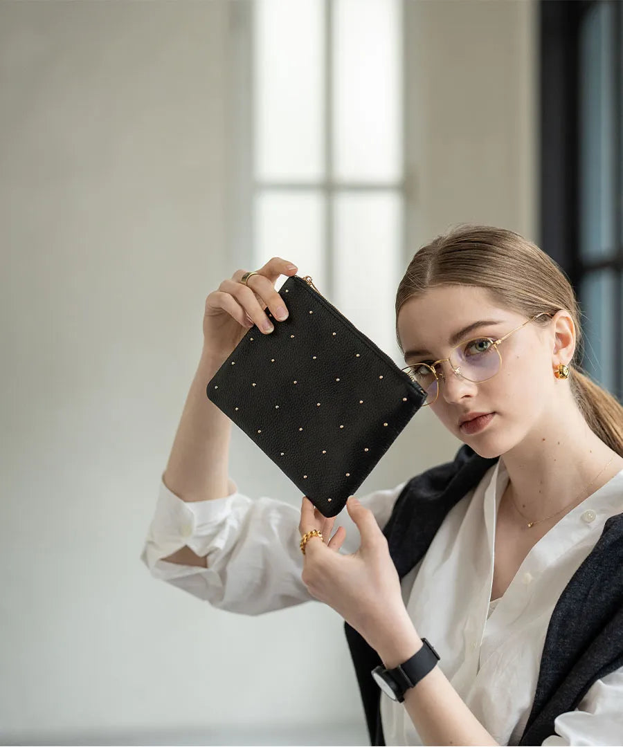 A female model is holding a leather pouch "Dotlpouch M" Color:Gold dot