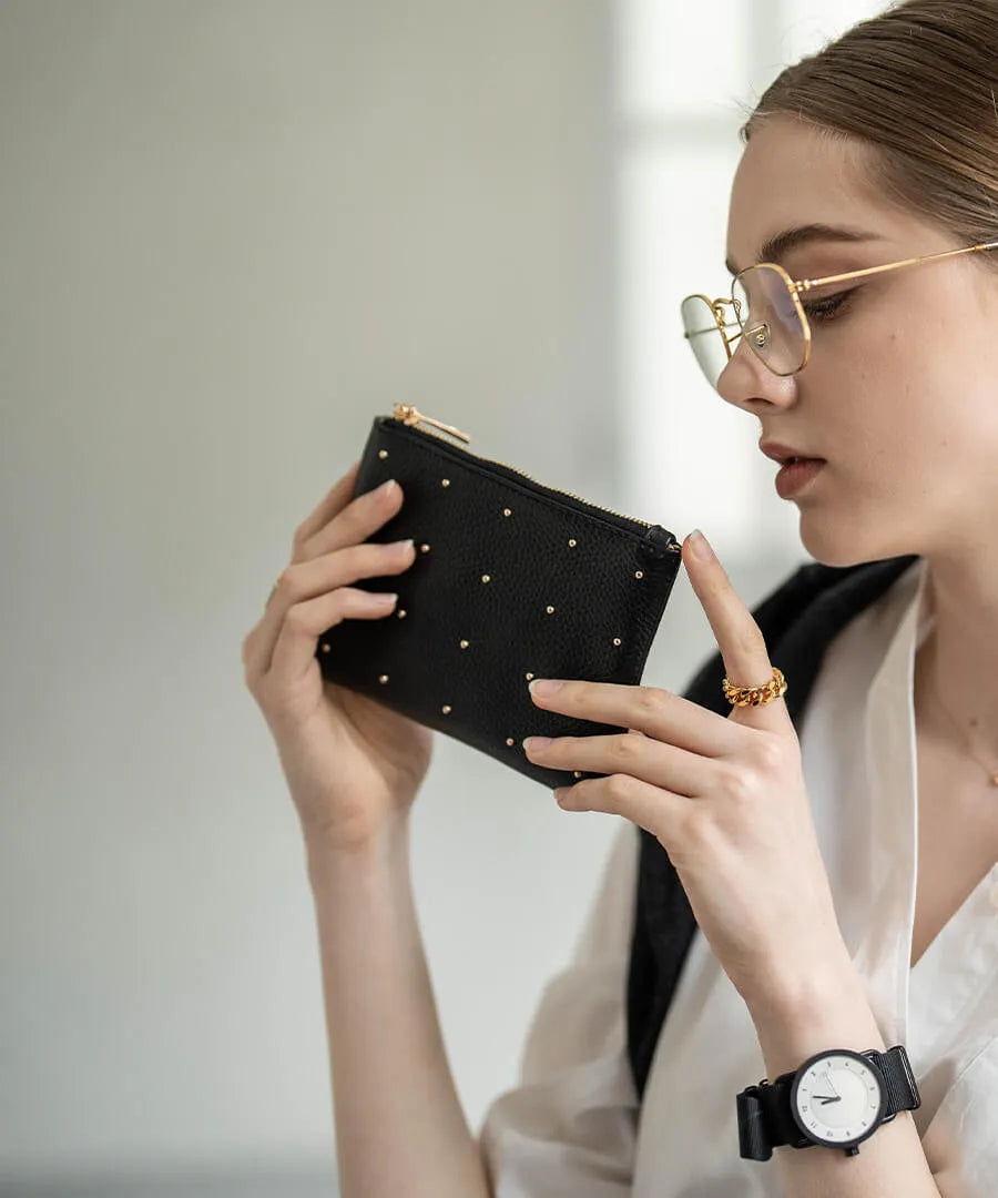 A female model is holding a leather pouch "Dotlpouch S" Color:Gold dot