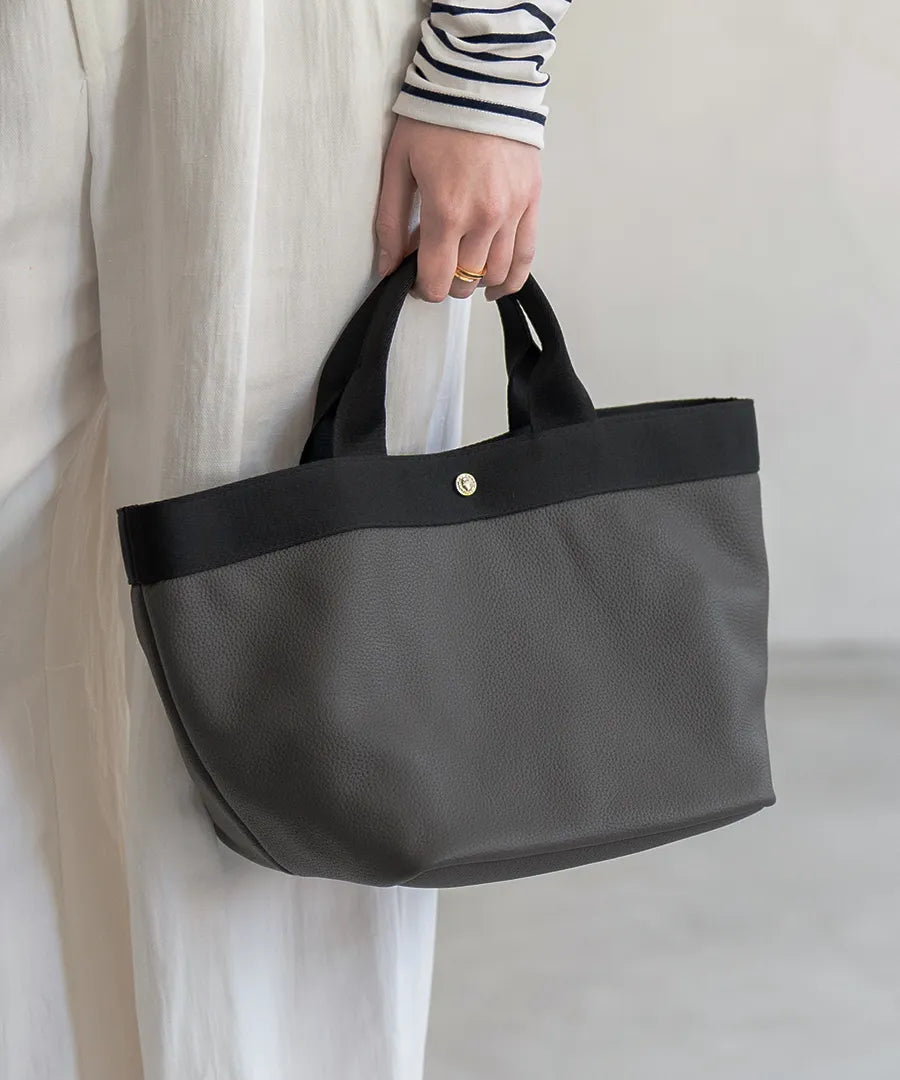 A female model is holding a tote bag "Emmalde" in colors: dark gray x black.