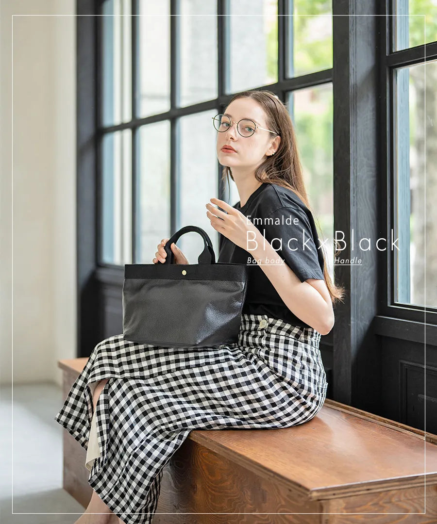 Colors of the female model sitting on a chair and the tote bag "Emalde": black x black.