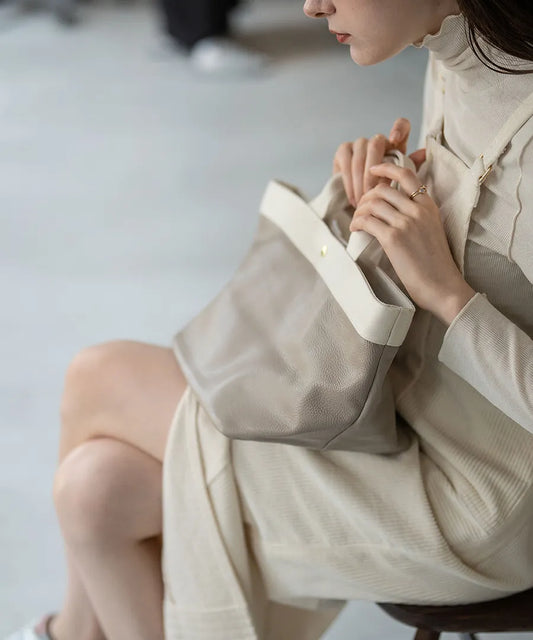 Colors of the female model sitting on a chair and the tote bag "Emalde": ivory x light gray.