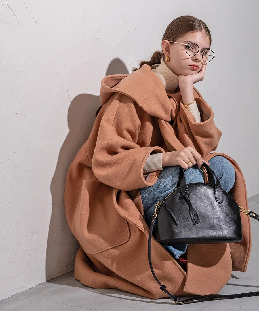 A female model is sitting and holding a tote bag "Ervi". Color: Black