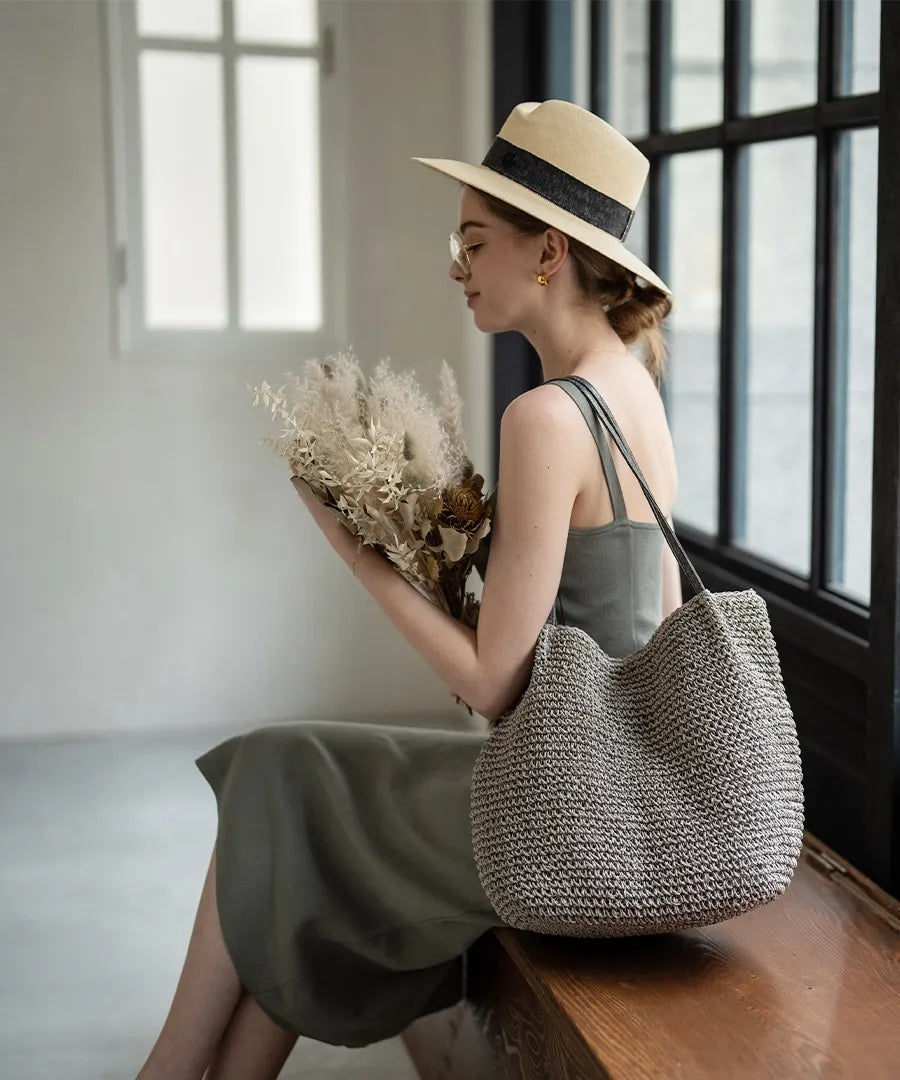 A female model is sitting and holding a tote bag "Garah".Color:Gray