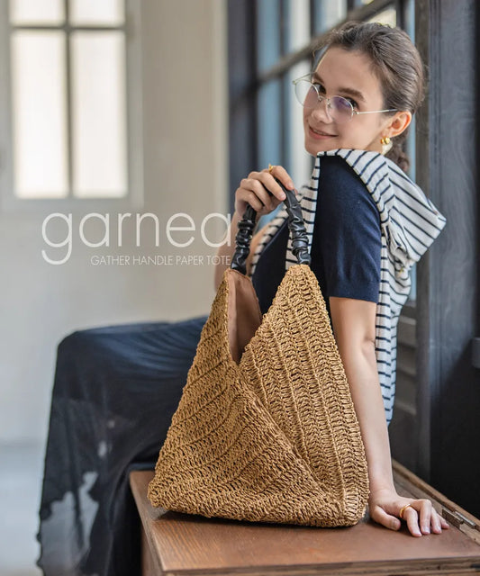 A female model is sitting and holding a tote bag "Garnea".Color:Natural camel