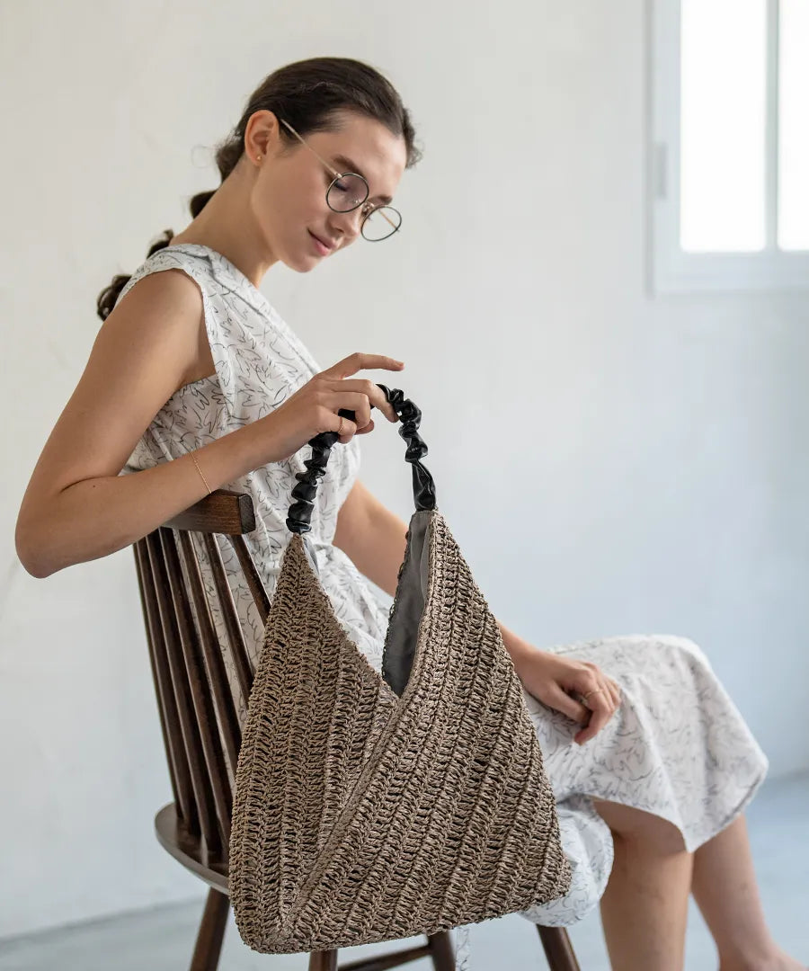 A female model is sitting and holding a tote bag "Garnea".Color:Gray