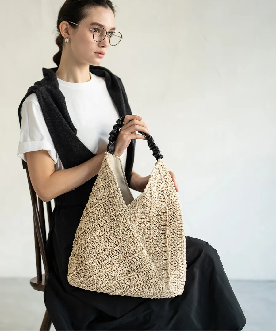 A female model is sitting and holding a tote bag "Garnea".Color:Natural beige