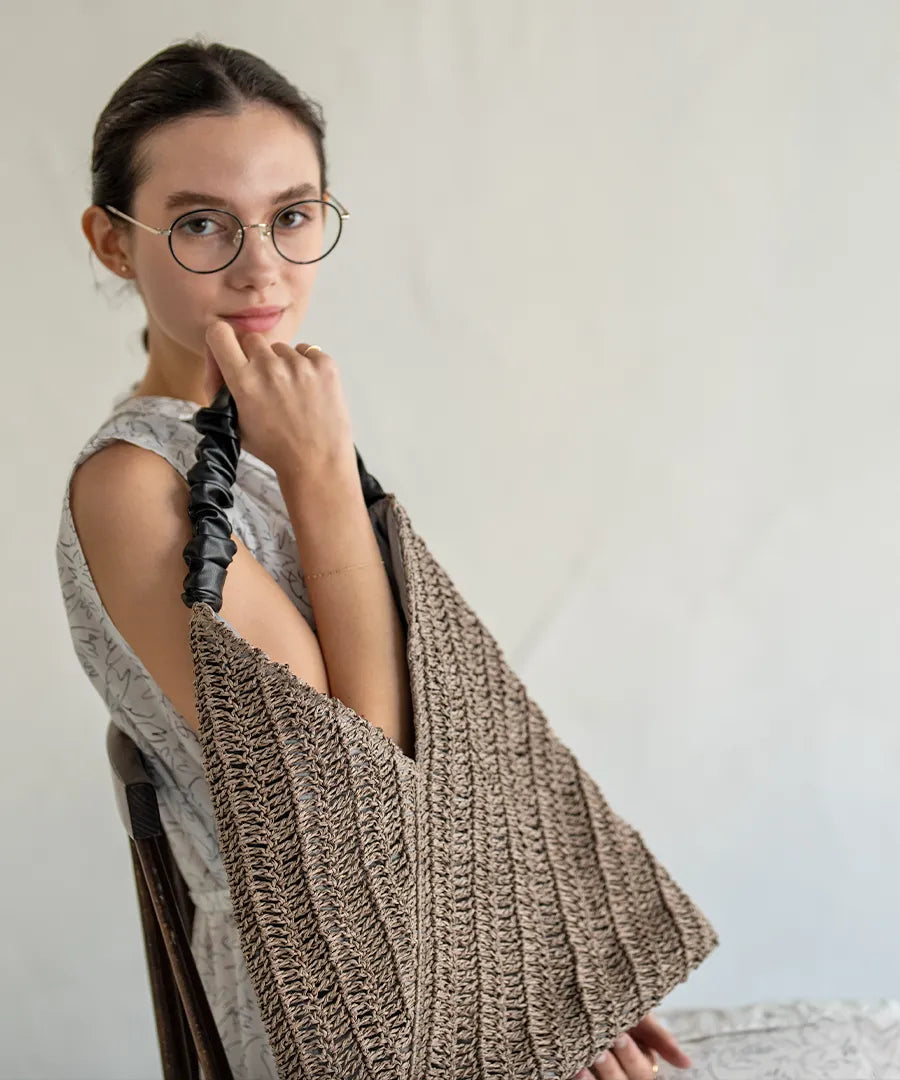 A female model is sitting and holding a tote bag "Garnea".Color:Gray