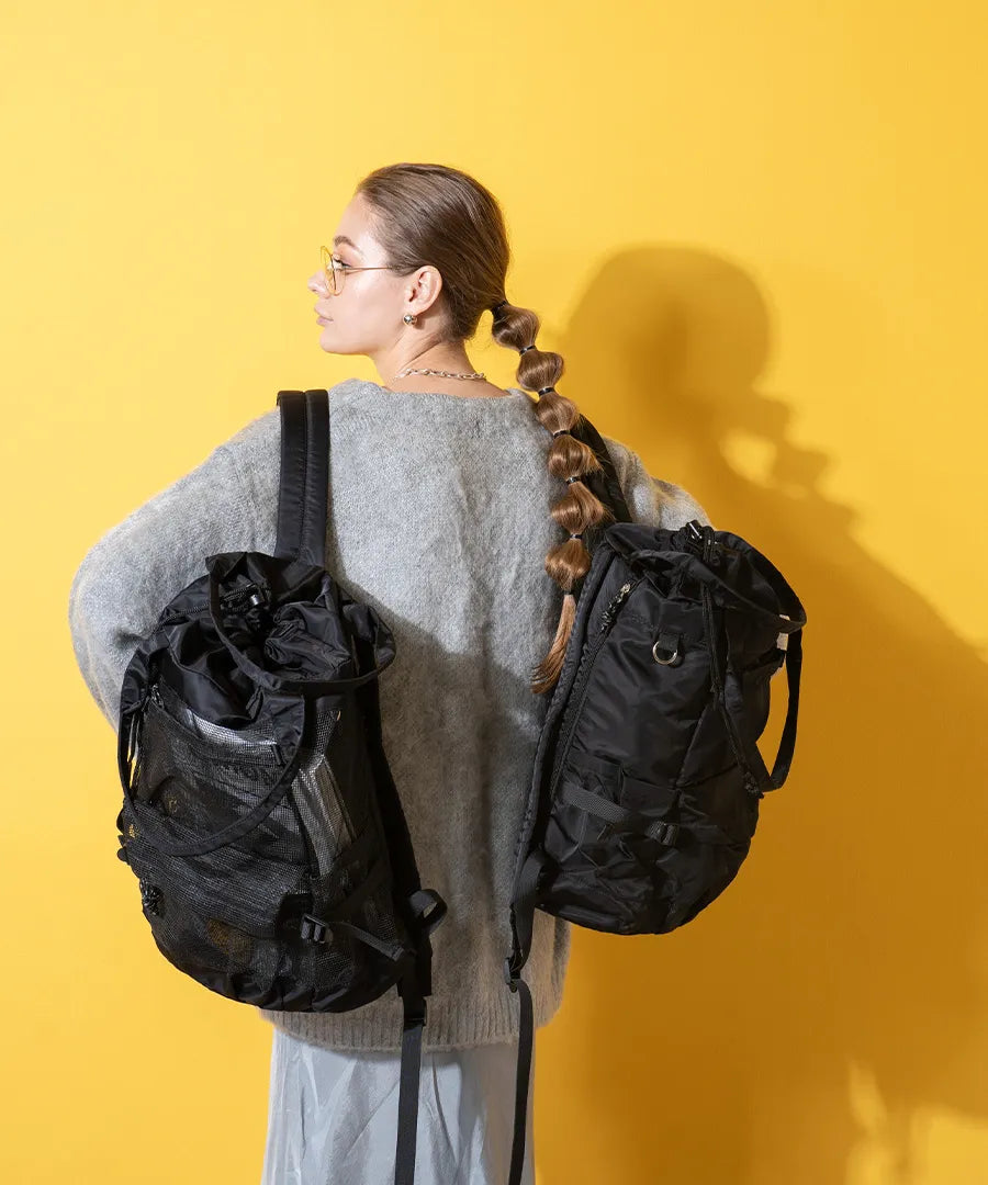 A female model is carrying a body bag "Glarca" over her shoulder.Color:Mesh black,Nylon black