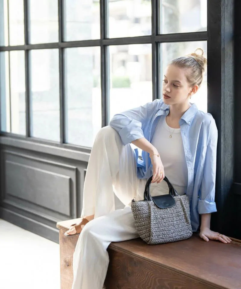 A female model is sitting and holding a hand bag "Glenda".Color:Gray × Black