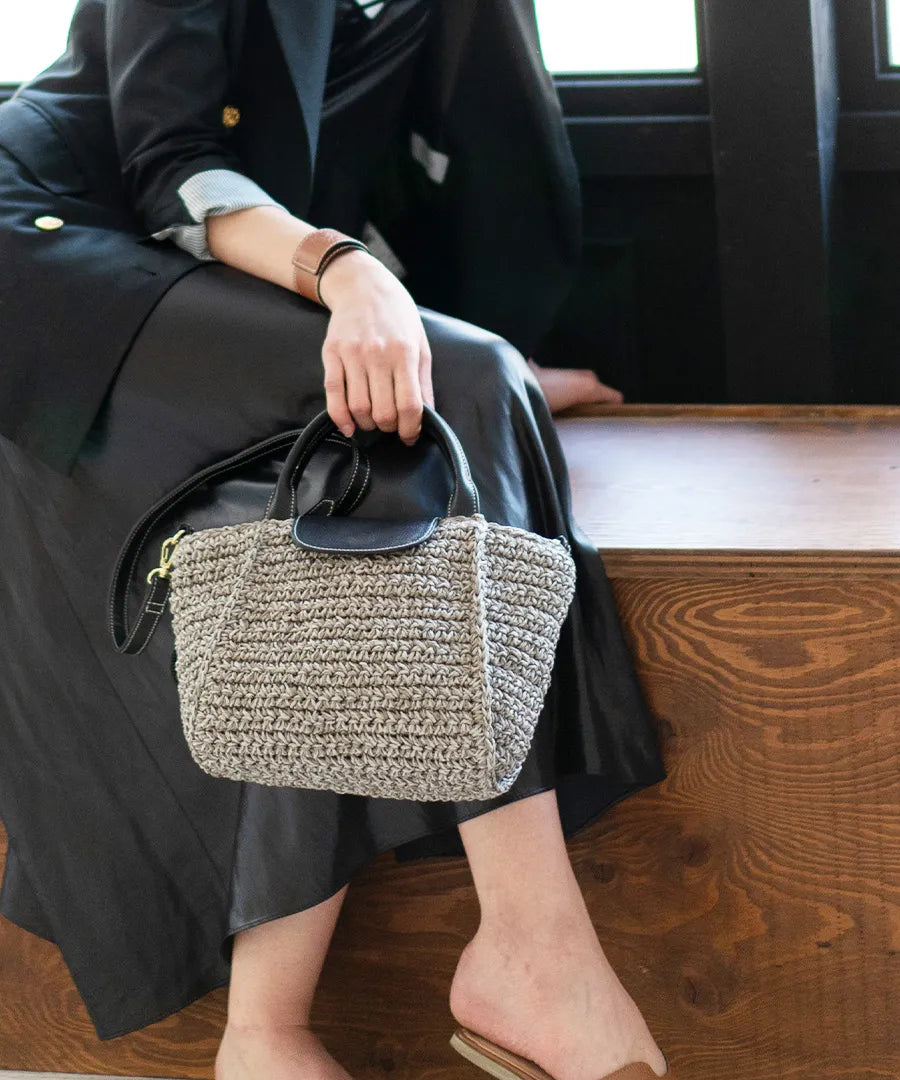 A female model is sitting and holding a hand bag "Glenda".Color:Gray × Black