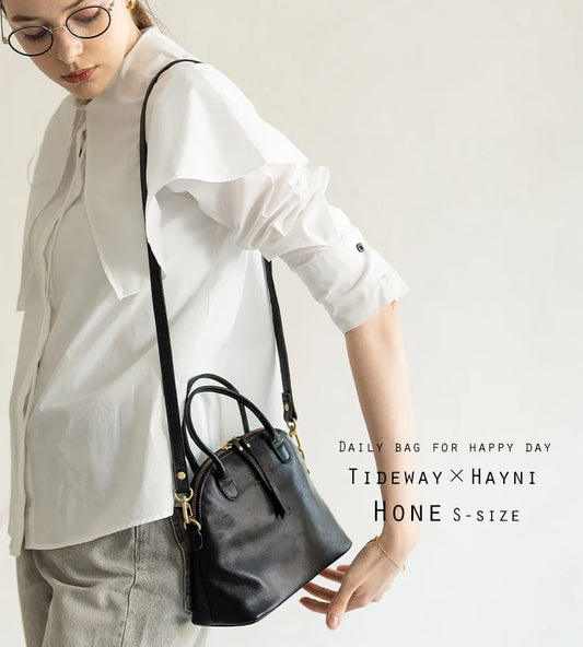 A female model is carrying a shoulder bag "Hone S-size (Version 2)" over her shoulder. Color:Black