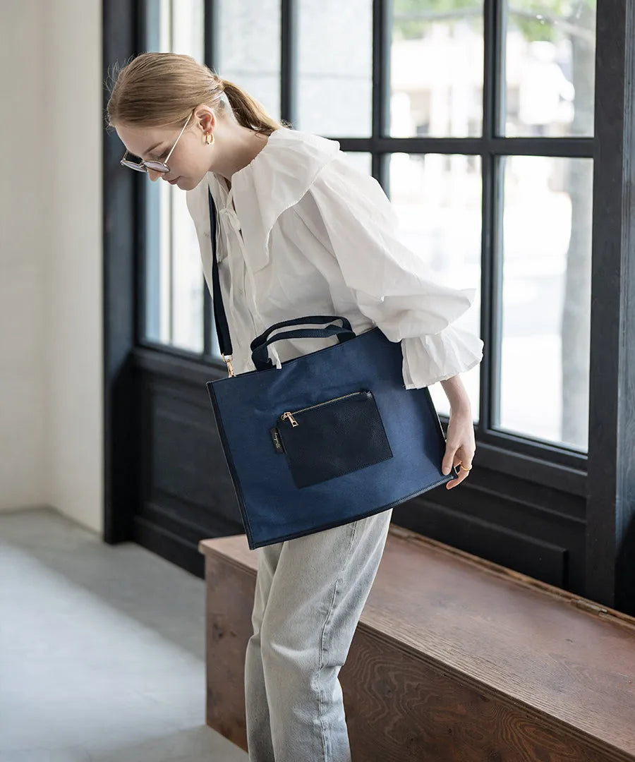 A female model is carrying a shoulder bag “Lesche” over her shoulder. Color:Navy