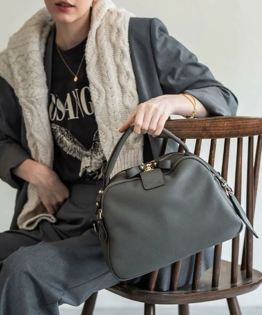 A female model is sitting and holding a hand bag "Mini Loche (Version 7)".Color:Elephant gray