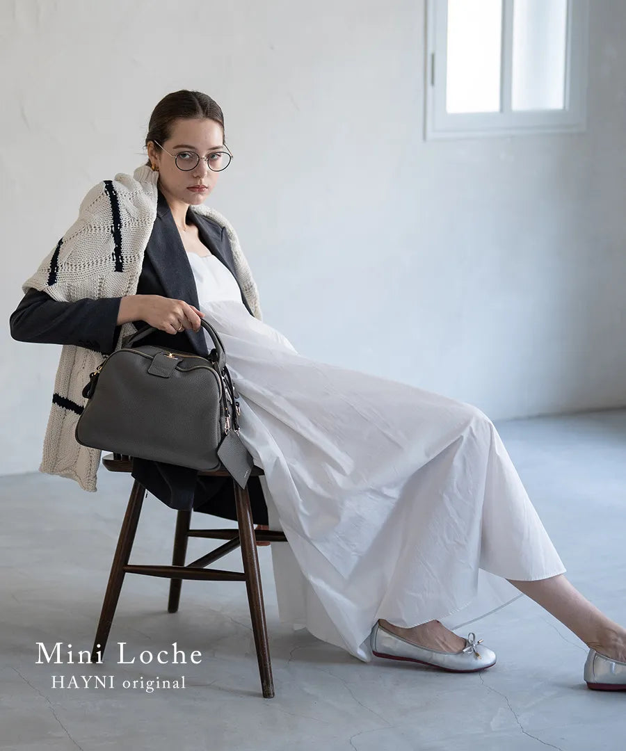 A female model is sitting and holding a hand bag "Mini Loche (Version 7)".Color:Elephant gray