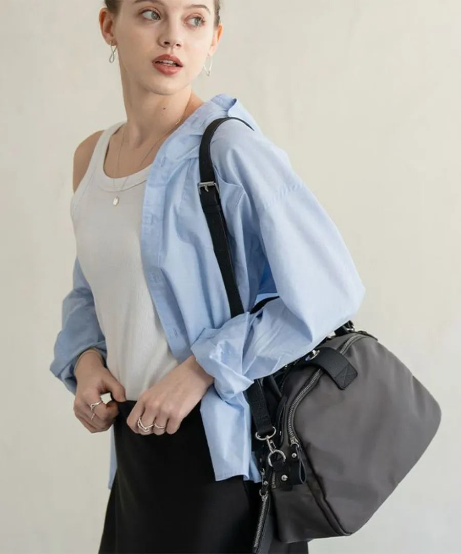 A female model is carrying a body bag "Mini Nylon Loche" over her shoulder.Color:Gray Black