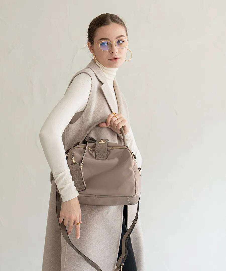 A female model is holding a hand bag "Mini Nylon Loche".Color:Greige