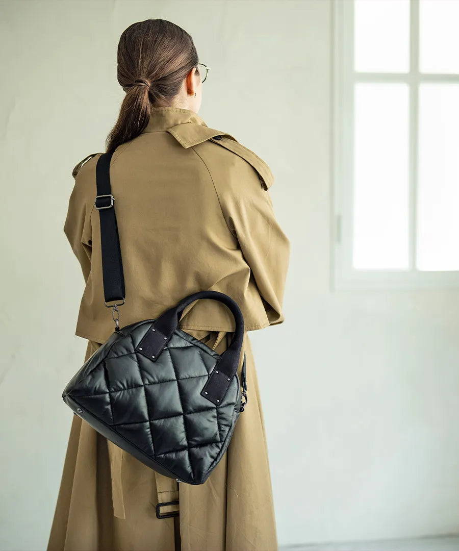 A female model is carrying a shoulder bag "Peremo (Version 2)" over her shoulder.Color:Black