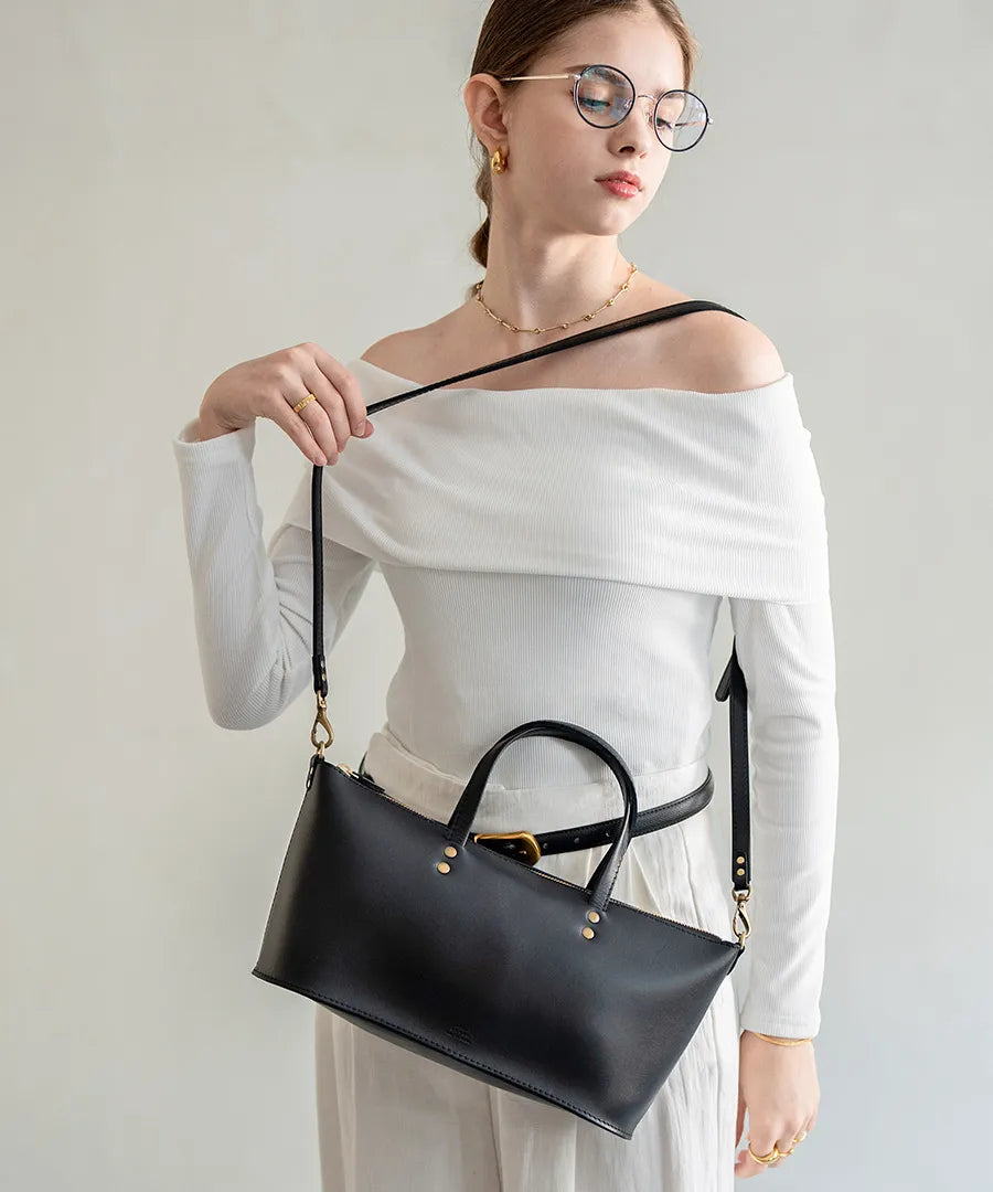 A female model is carrying a shoulder bag "Recte" over her shoulder. Color:Black