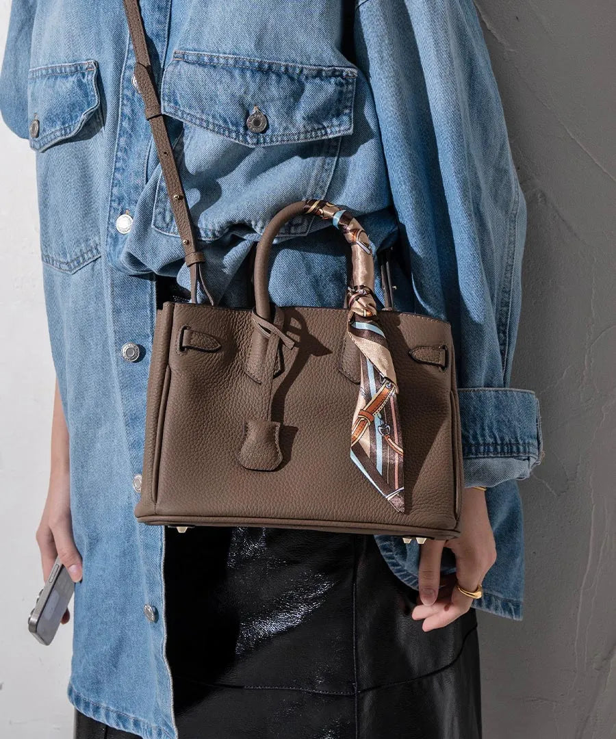 A female model attaches a scarf to the handle of the bag and carries the bag over her shoulder.