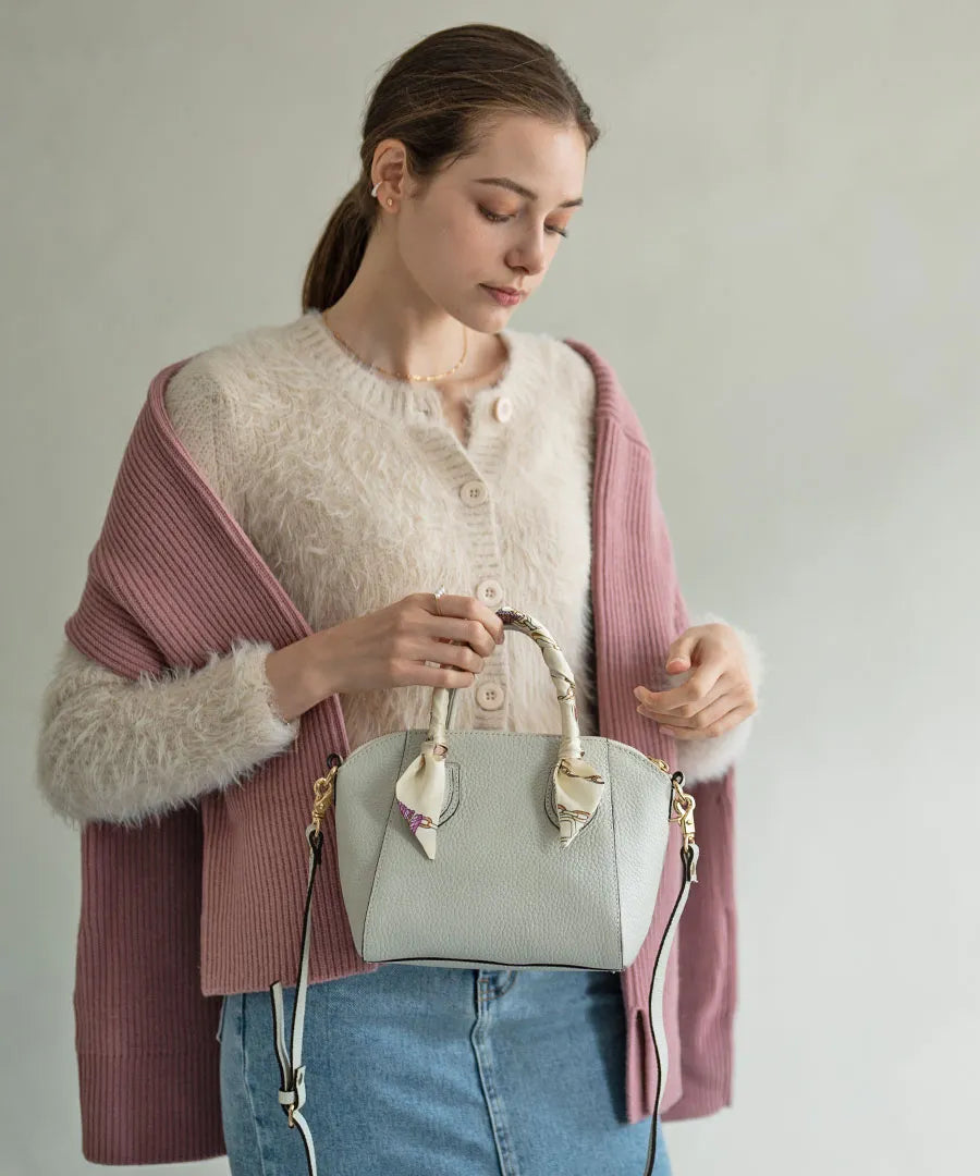 A female model attaches a scarf to the handle of the bag and holds the bag in her hand.