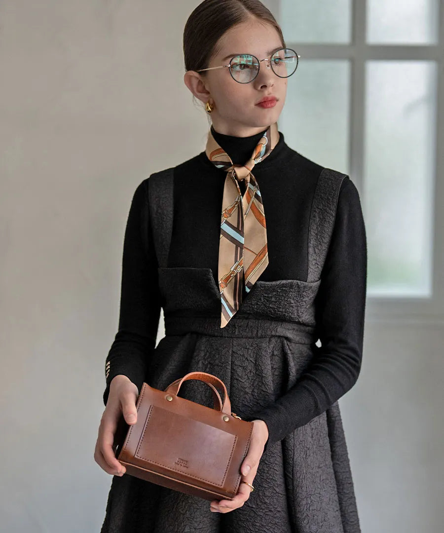 A female model is wearing a scarf around her neck and holding a bag in her hand.