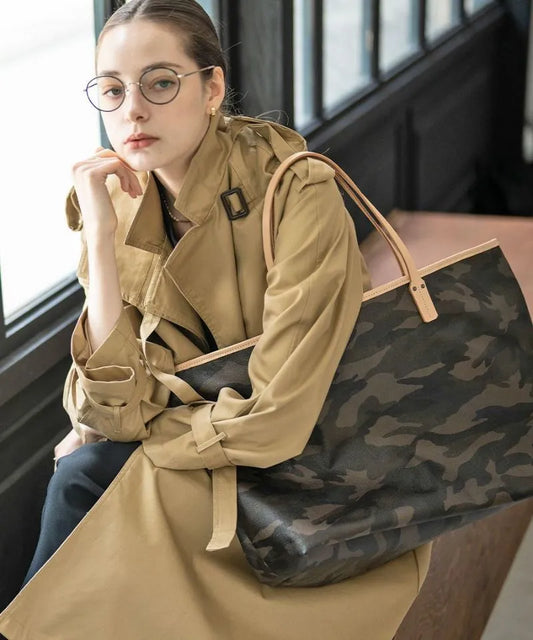 A female model is sitting and holding a tote bag "Yutka L".Color:Camouflage